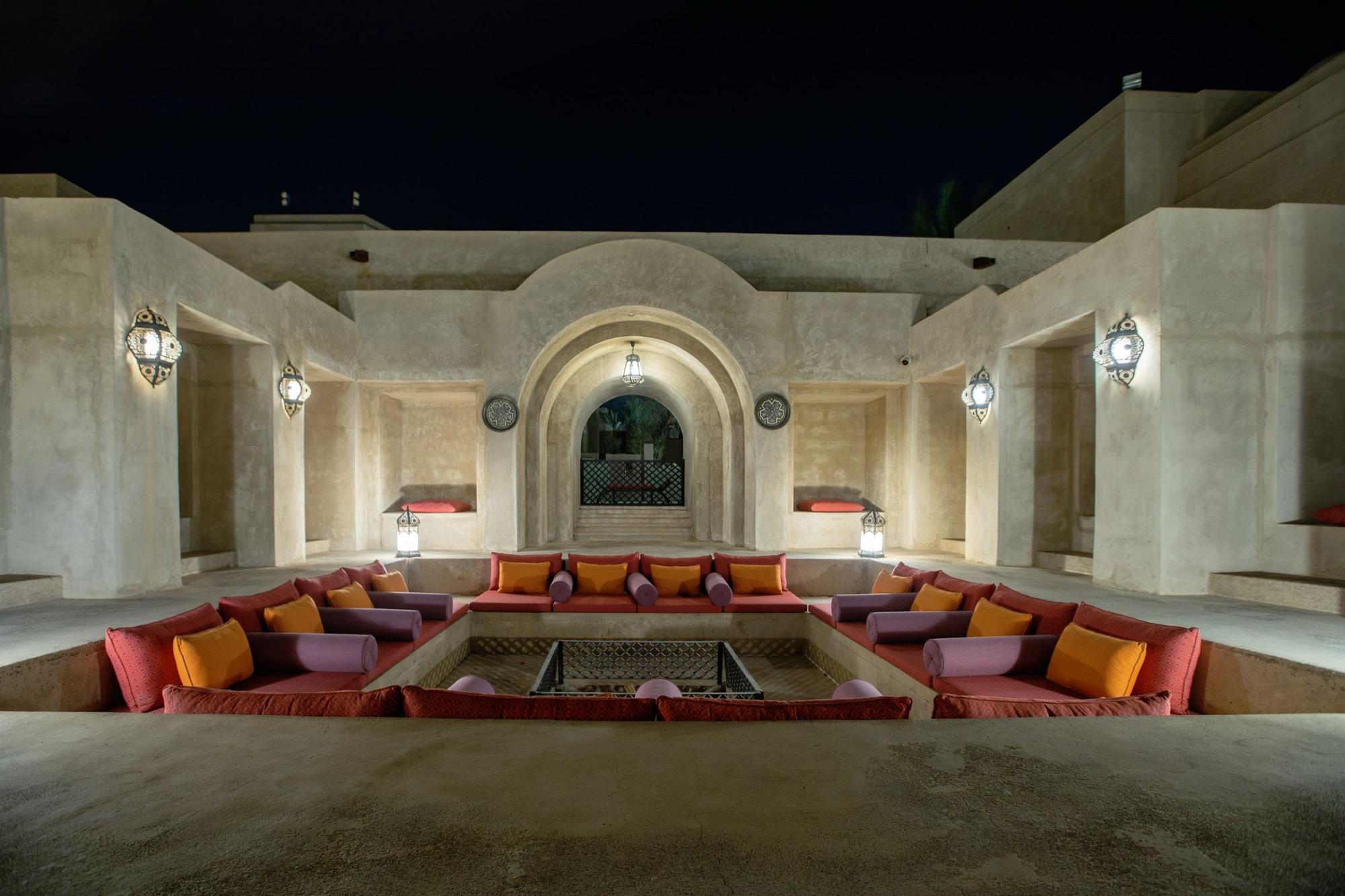 Night courtyard of a desert house, with arched stone seating around a low fire