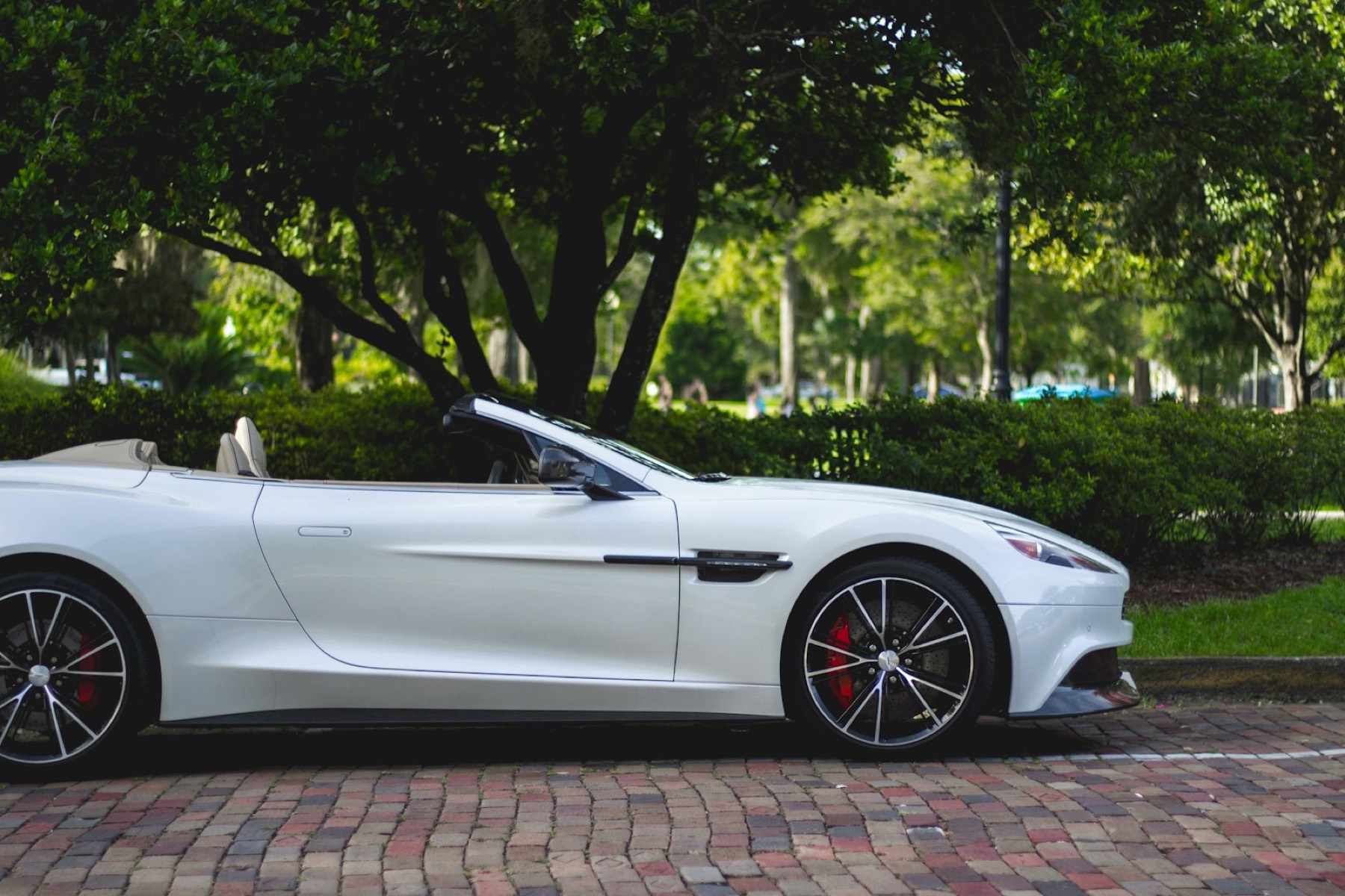 A white convertible parked under trees on a brick street