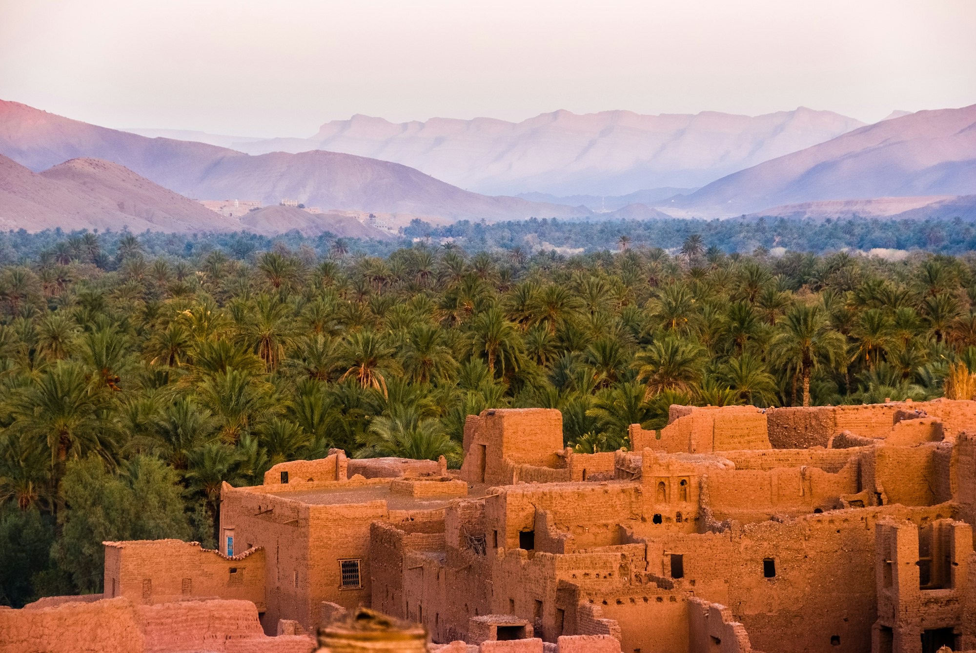 An earthen village above a palm grove, with desert mountains beyond