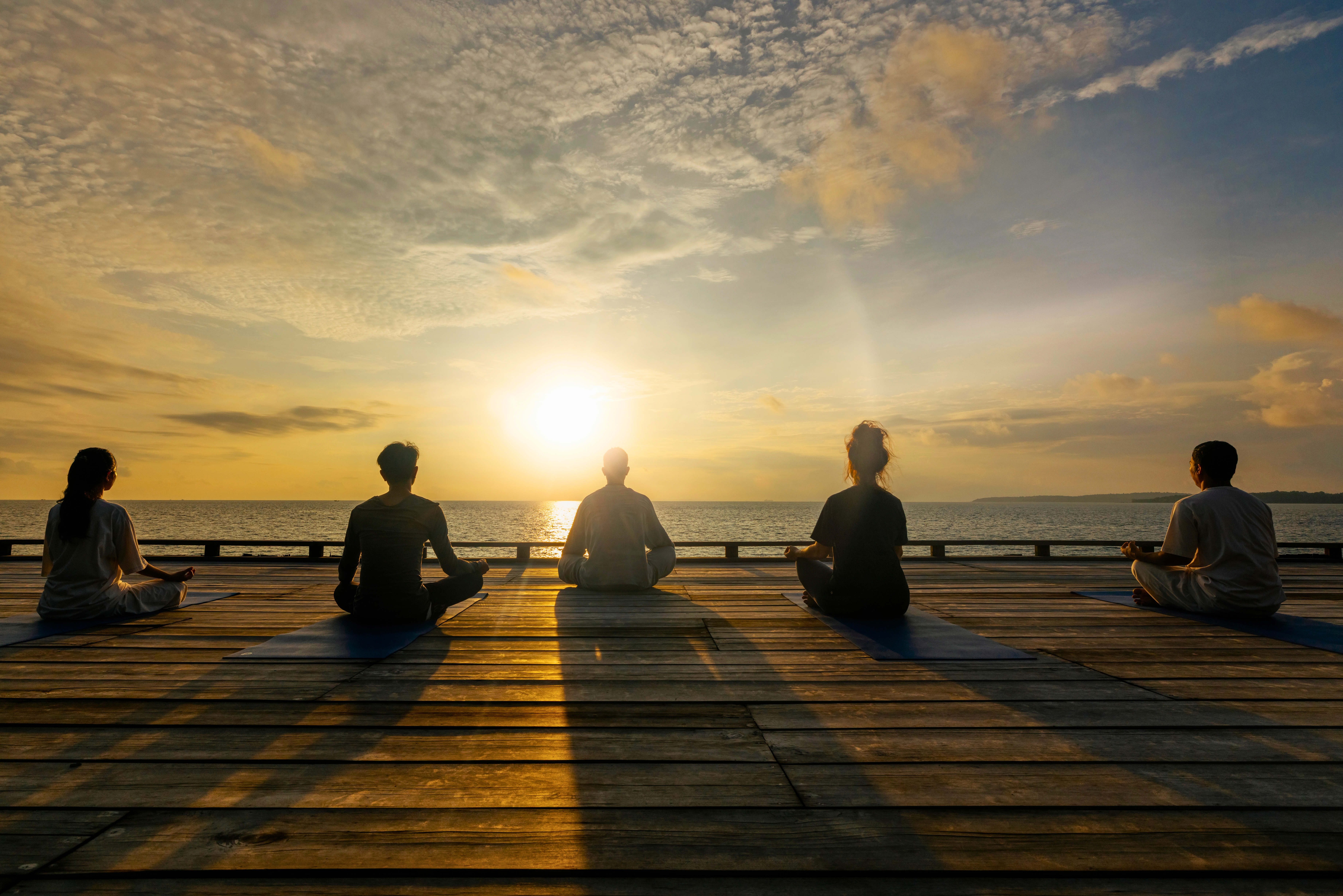 Team practicing yoga at sunset overlooking the ocean